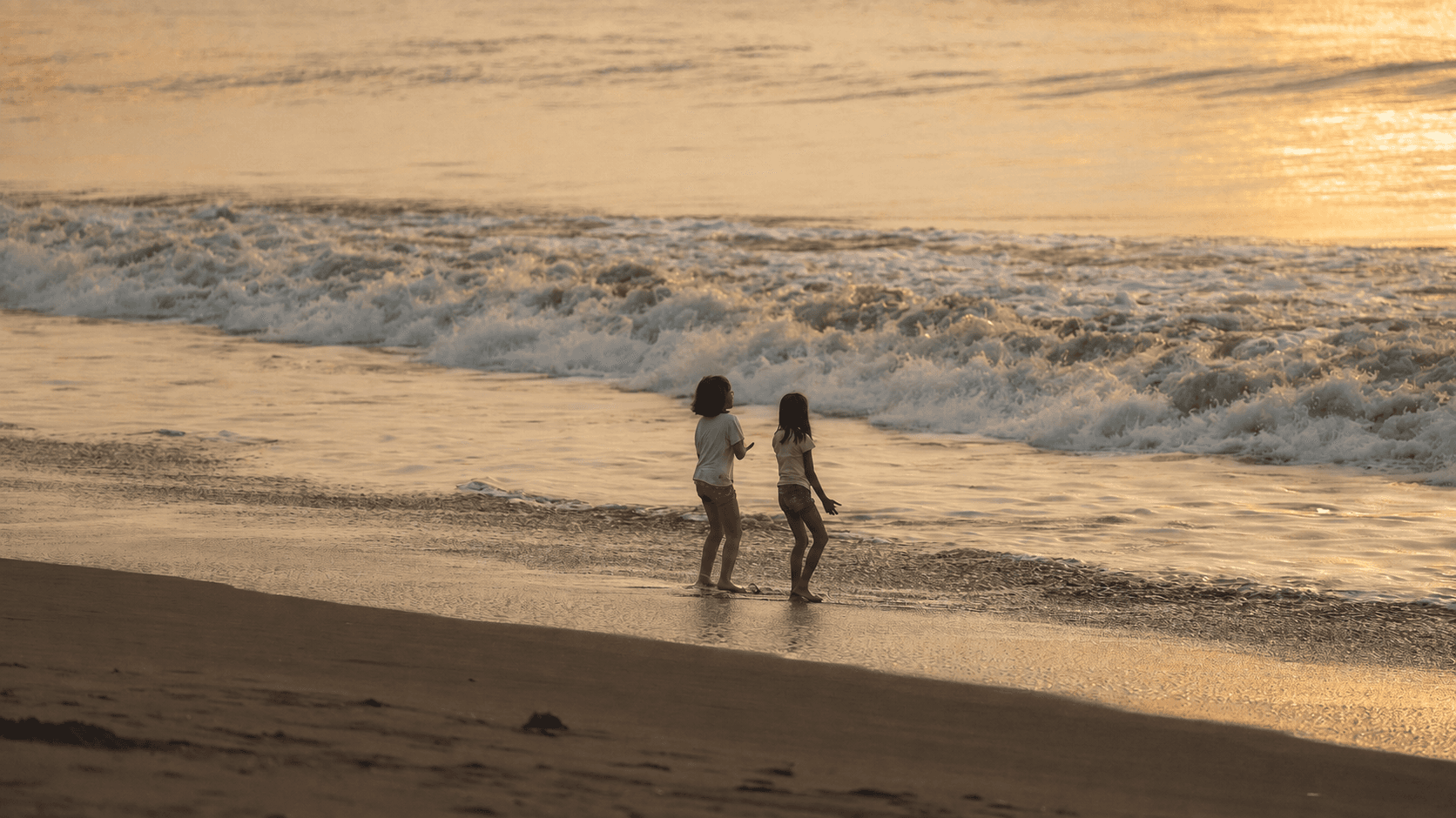 Two children standing at the water’s edge on a Sanur beach at sunrise